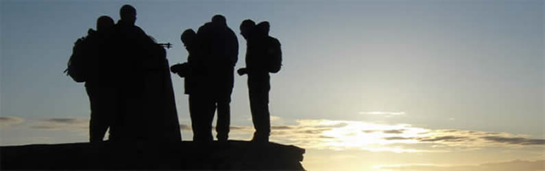Jubilant group standing beside summit trig point on Ben Nevis as dawn is breaking